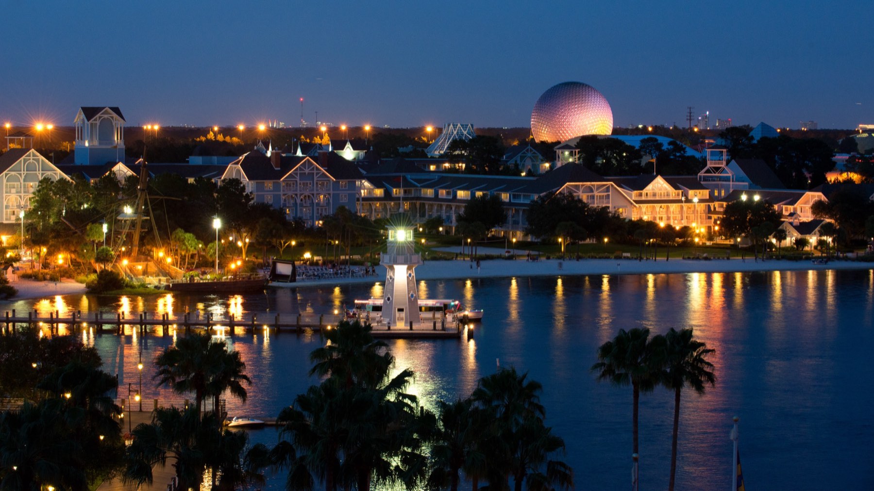Resort hotels around a lake at dusk with Spaceship Earth lit up behind them