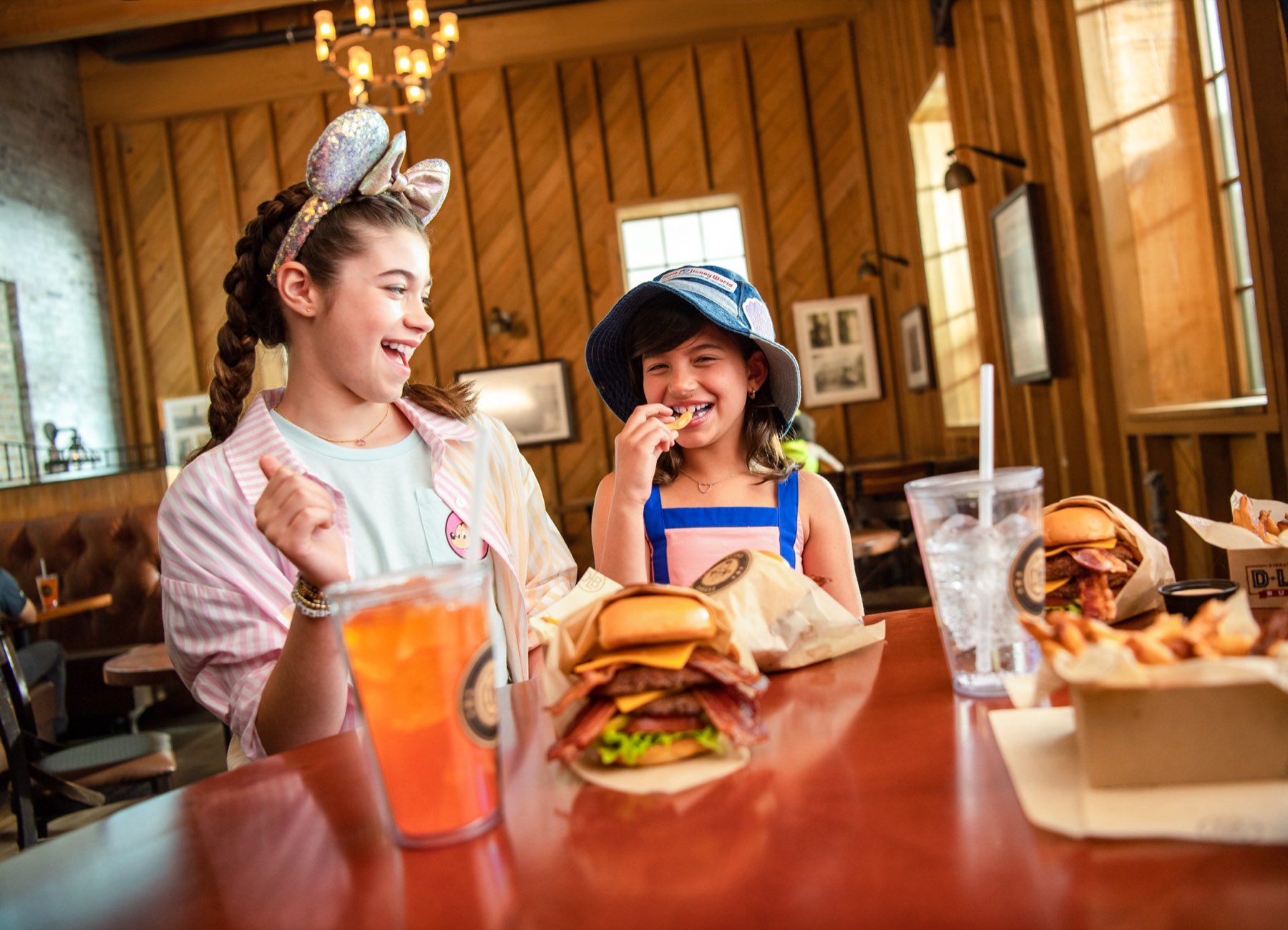 Two kids laughing over burgers and fries at a wooden table